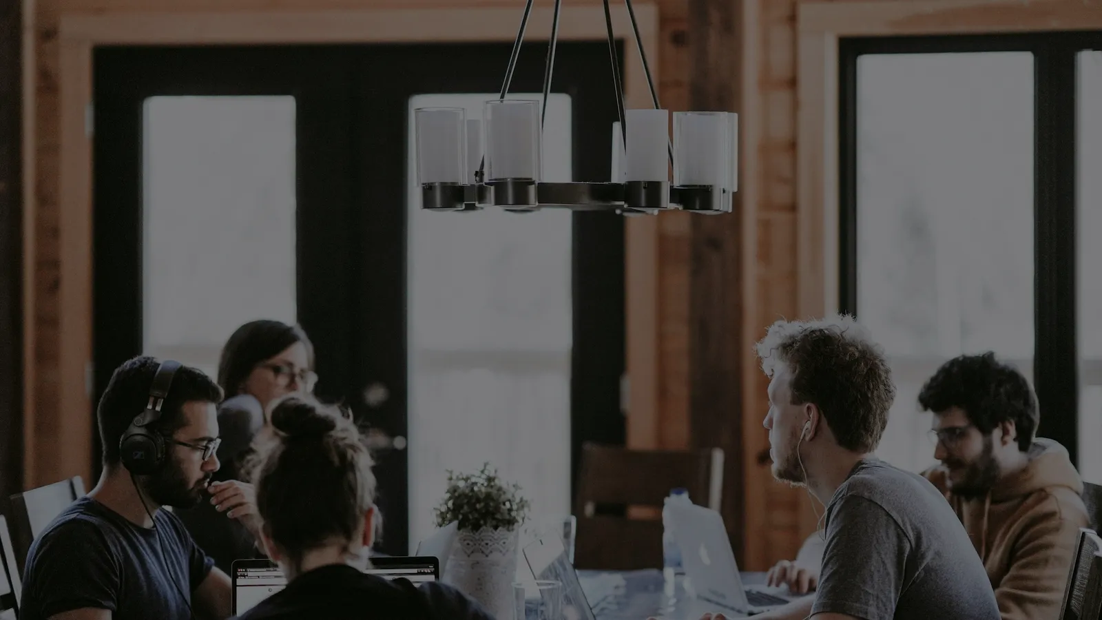 Équipe réunie autour d’une grande table de travail dans un bureau lumineux, ordinateurs ouverts et échanges en cours.