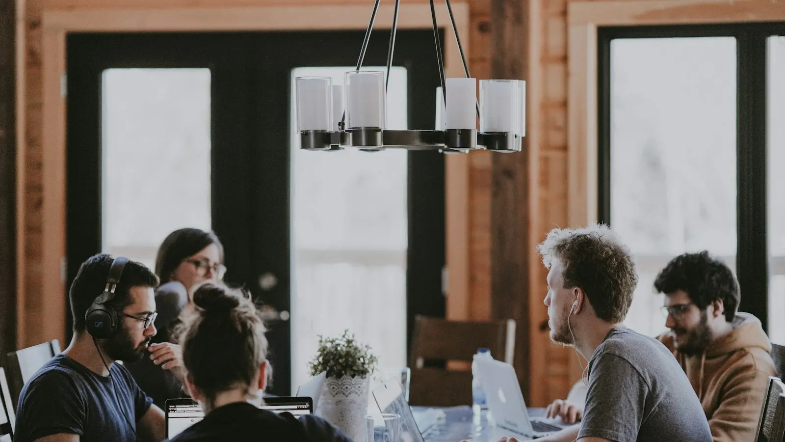 Équipe réunie autour d’une grande table de travail dans un bureau lumineux, ordinateurs ouverts et échanges en cours.