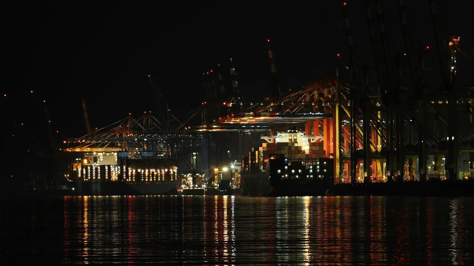 Terminal à conteneurs éclairé la nuit, portiques et porte-conteneurs à quai, évoquant le transit de marchandises entre juridictions.