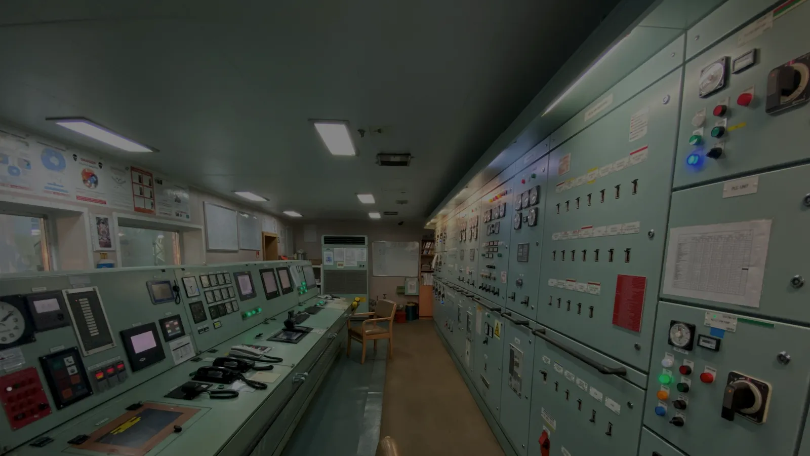 Salle de contrôle occupée par des pupitres couverts d’interrupteurs, de cadrans et de voyants, sous un éclairage bas.