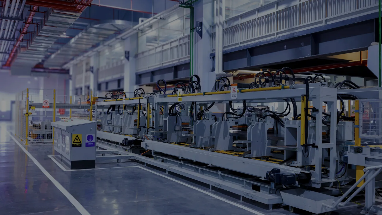 Ligne de production automatisée dans une halle industrielle : stations de travail identiques alignées le long d’un convoyeur, barrières de sécurité et marquages au sol.