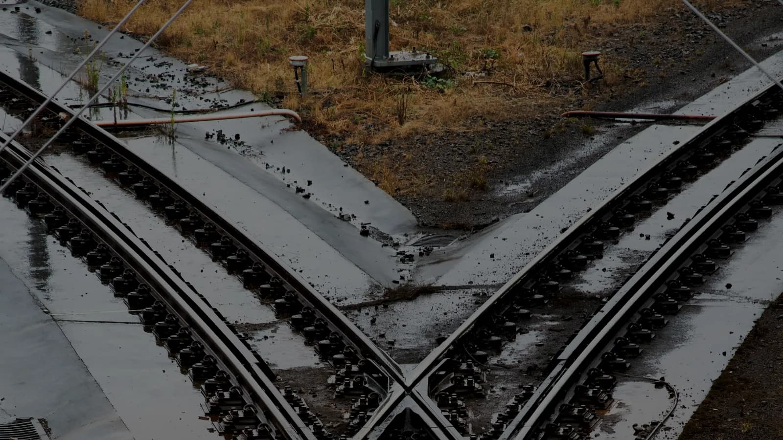 Deux voies ferrées se séparant depuis un même point, les rails mouillés dessinant deux trajectoires divergentes sur le ballast sombre.
